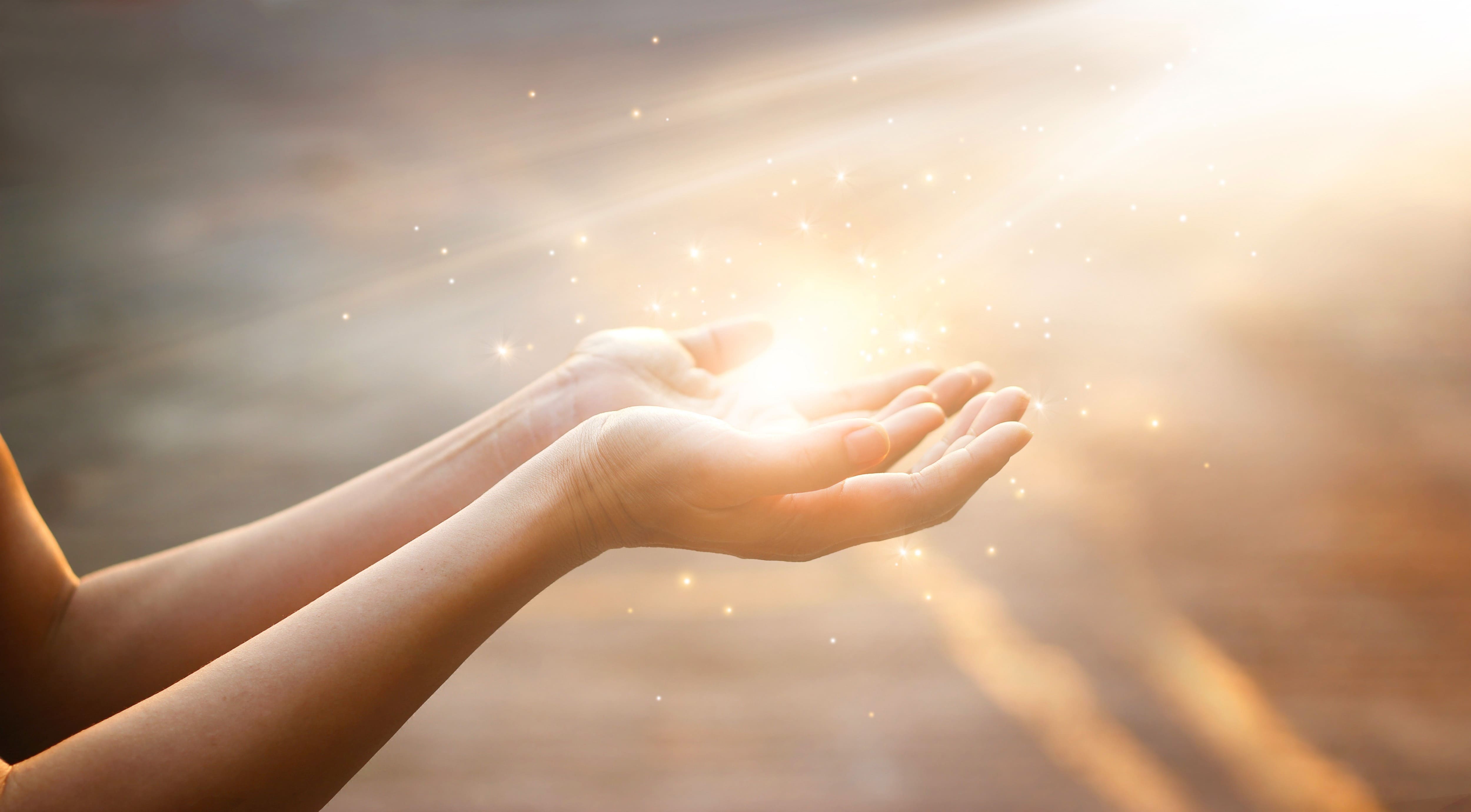 geöffnete hände mit einem lichtstrahl der nach oben zeigt